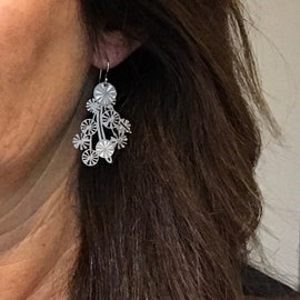 Close-up of a person wearing silver floral earrings with long brown hair.