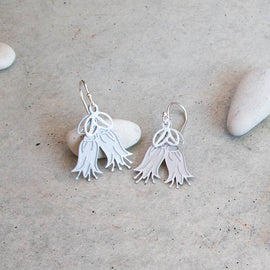Silver earrings on a textured beige surface with stones in the background