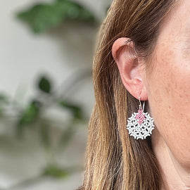Close-up of a person wearing snowflake-shaped earrings with a blurred green plant background