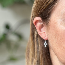 Close-up of a person wearing a silver earring with a blurred natural background