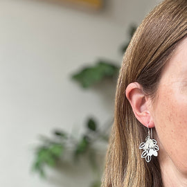 Close-up of a person wearing silver floral earrings with a blurred background