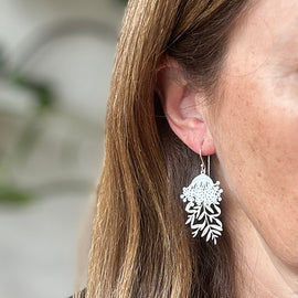 Close-up of a person wearing silver leaf-shaped earrings with a blurred background