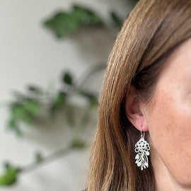 Close-up of a person wearing a silver earring with a blurred green plant background