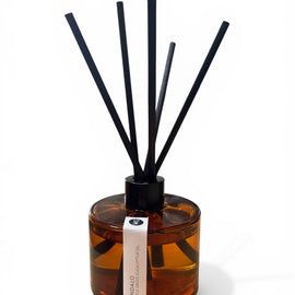 Reed diffuser with black reeds in an amber bottle on a white background