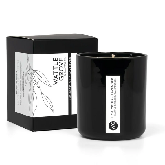 Black candle with Wattle Grove branding next to its packaging on a white background