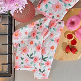 Floral-patterned towels on a kitchen counter with pink donuts and a vase of flowers.
