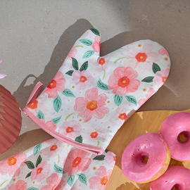 Floral oven mitt on a table with pink frosted donuts and flowers.