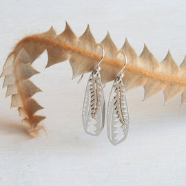 Silver feather-shaped earrings on a white background with dried leaves.
