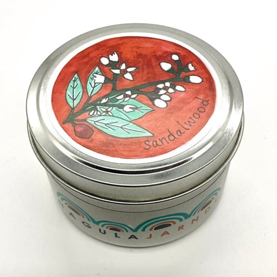 Candle in a tin container with a decorative lid featuring sandalwood design on a white background