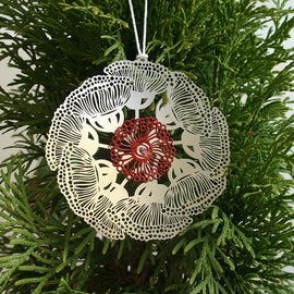 A round, red stainless steel Christmas ornament with a floral pattern, featuring a powder-coated finish and tied with string.