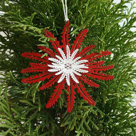 A metal Christmas ornament shaped like a Banksia leaf with a red and silver color scheme, with a string attachment.