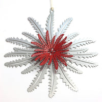 A metal Christmas ornament shaped like a Banksia leaf with a red and silver color scheme, with a string attachment.