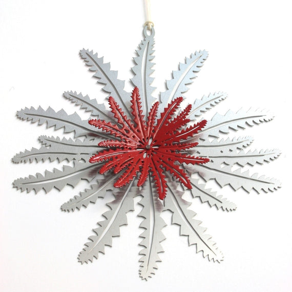 A metal Christmas ornament shaped like a Banksia leaf with a red and silver color scheme, with a string attachment.